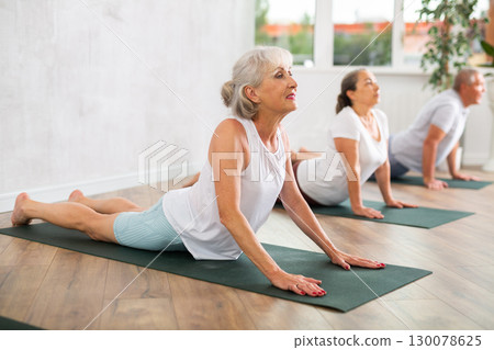 Mature women of different year practice yoga and Pilates in virabhadrasana pose in gym 130078625