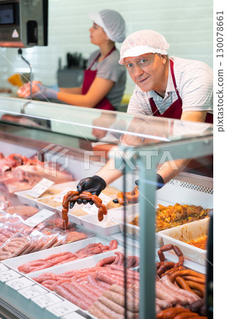 Male seller leans over to refrigerator window and takes out some raw barbecue sausages for buyer Male seller leans over to refrigerator window and takes out some raw barbecue sausages for buyer 130078661