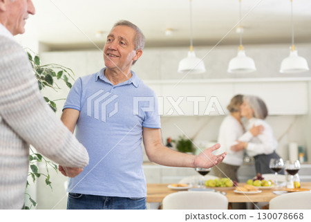 Two men smiled and greeted each other with a firm handshake before taking their seats at beautifully set dinner table 130078668