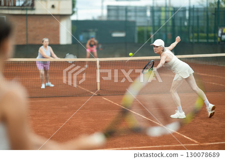 Aged woman enthusiastically playing tennis outdoors in summer 130078689