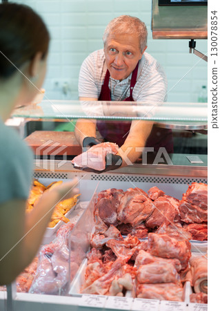 Senior male seller offers girl to buy fresh pork entrecote boneless meat 130078854