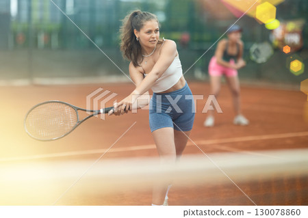 Two young women playing doubles tennis Two young women playing doubles tennis 130078860
