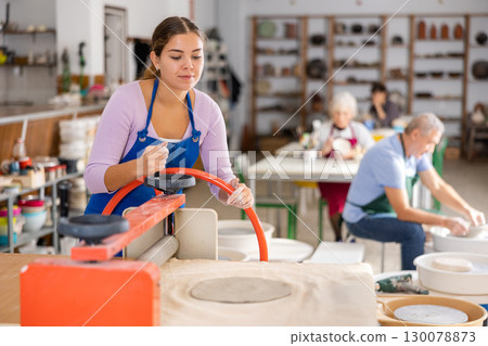 Young woman rolls out clay on craft machine clay press roller in studio 130078873