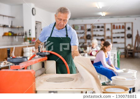 Old man rolling piece of clay on special machine - craft machine clay press roller 130078881