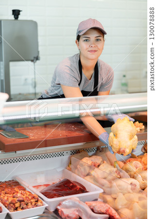 Young saleswoman laying raw broiler chickens in display case 130078888