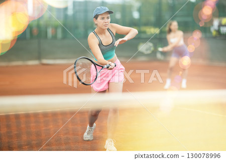 Two young women playing doubles tennis Two young women playing doubles tennis 130078996