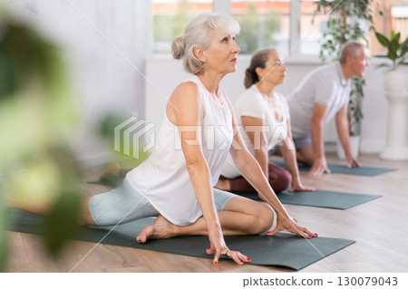 Elderly women practicing yoga in virabhadrasana pose in gym Elderly women practicing yoga in virabhadrasana pose in gym 130079043
