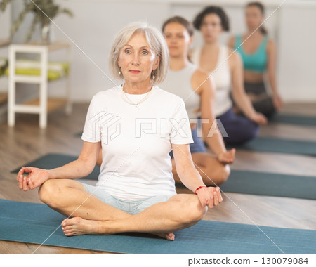 Elderly woman doing yoga in group in studio 130079084