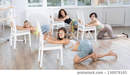 Girl with unfastened hair sitting on floor and leaning on chair, performing lap dance in high heels 130079105