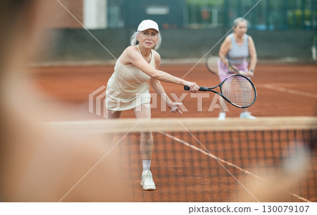 Elderly woman engrossed in doubles tennis game on clay court 130079107