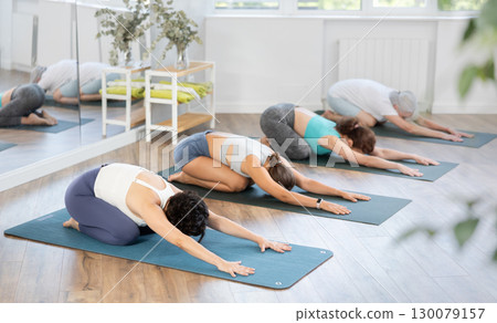 Downward facing dog yoga pose - positive women doing yoga in fitness gym 130079157