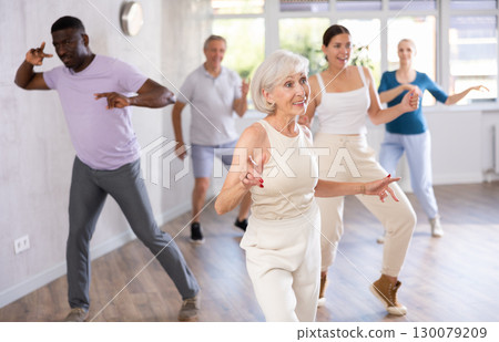 Senior lady dancing twist during group training in dance studio Senior lady dancing twist during group training in dance studio 130079209