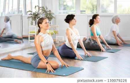 Group of women practicing pigeon pose of yoga on mat in fitness room 130079226