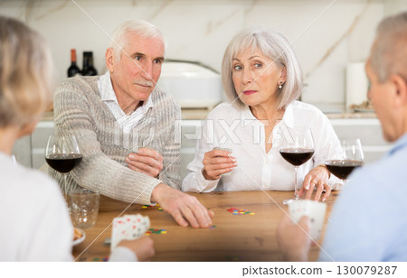 Cheerful friendly company of men and women sitting at kitchen table and enjoying the poker game. Friends play card game at home. Evening entertainment concept Cheerful friendly company of men and women sitting at kitchen table and enjoying the poker game. Friends play card game at home. Evening entertainment concept 130079287