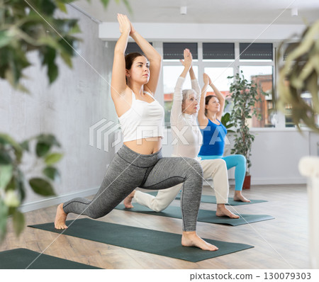 Smiling women training yoga positions in modern yoga studio Smiling women training yoga positions in modern yoga studio 130079303