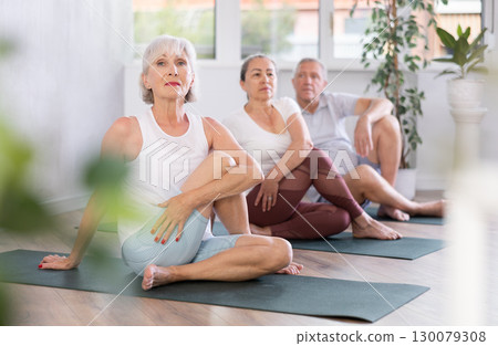 Focused mature woman performs Lord of Fishes asana by Ardha Matsyendrasana Focused mature woman performs Lord of Fishes asana by Ardha Matsyendrasana 130079308