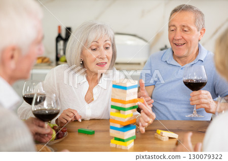 Group of four mature friends is playing board game with wooden blocks in kitchen 130079322