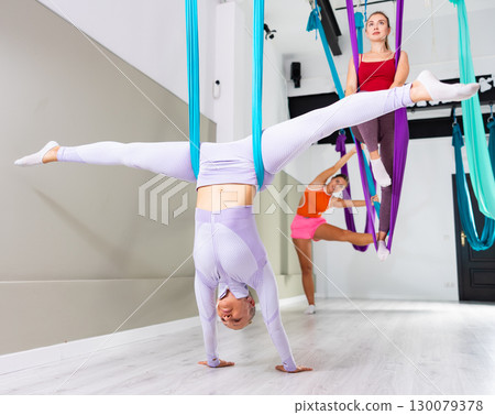 Woman doing split in handstand position supported by aerial yoga hammock Woman doing split in handstand position supported by aerial yoga hammock 130079378