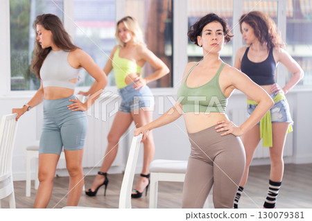 Group of women in high heels rehearsing dance while leaning on chair 130079381