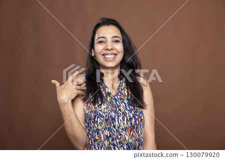 Portrait of happy indian woman with long hair and casual clothing, confidently smiling and gesturing with hand. Gorgeous female model with joyful energy radiating positivity in brown background studio Portrait of happy indian woman with long hair and casual clothing, confidently smiling and gesturing with hand. Gorgeous female model with joyful energy radiating positivity in brown background studio 130079920