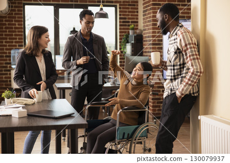 Professional employees having a lighthearted conversation, promoting teamwork in a business setting. Cheerful asian woman in a wheelchair chatting with her inclusive team, taking a short break. Professional employees having a lighthearted conversation, promoting teamwork in a business setting. Cheerful asian woman in a wheelchair chatting with her inclusive team, taking a short break. 130079937