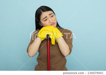 Bored female janitor leaning on mop, overwhelmed by cleaning duties. Exhausted asian housekeeper resting on broomstick, drained from repetitive household chores and long hours of service. Bored female janitor leaning on mop, overwhelmed by cleaning duties. Exhausted asian housekeeper resting on broomstick, drained from repetitive household chores and long hours of service. 130079941