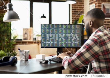 Focused entrepreneur working from home, analyzing stock market and planning profitable investment strategies for startup business. Man seated at desk reviewing forex trading trends with concentration. 130080020