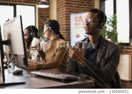 African american male employee in modern workspace, listening attentively through a headset while assisting a client. Black man talking to remote customer, providing technical support. African american male employee in modern workspace, listening attentively through a headset while assisting a client. Black man talking to remote customer, providing technical support. 130080051