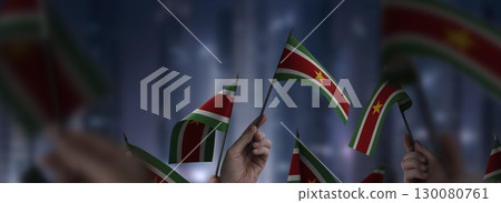 Suriname flags in their hands on a blurred urban background 130080761