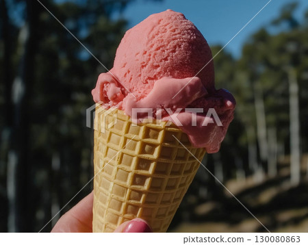Enjoying a delicious strawberry ice cream cone in a sunny park setting 130080863