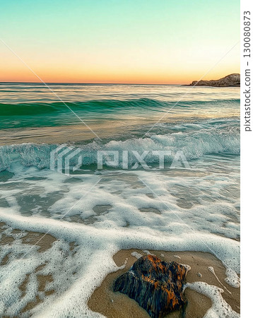 Sunset over tranquil beach with gentle waves lapping at the shore 130080873