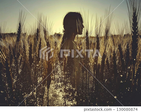 Silhouette of a woman standing in a wheat field during sunset near a rural area 130080874