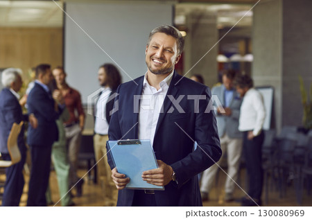 Happy confident business man looking at the camera and smiling in the office. Happy confident business man looking at the camera and smiling in the office. 130080969