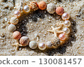 Elegant bracelet made of pearls and seashells resting on a sandy beach in sunlight 130081457