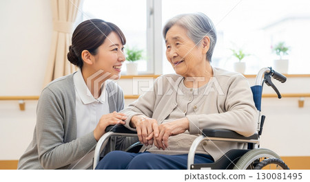 A young caregiver smiling gently at a senior woman in a wheelchair 130081495