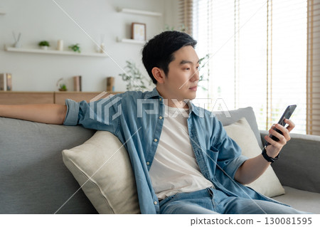 Smiling handsome young Asian man sitting on cozy couch 130081595