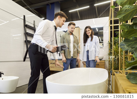 A salesman in a plumbing store helps a couple choose a bathtub 130081815