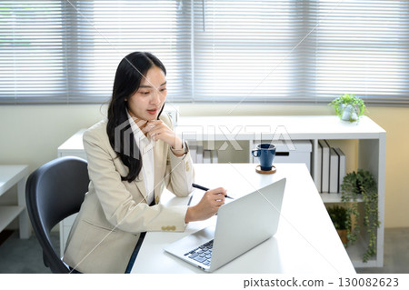 Confident female entrepreneur in blazer using computer for business planning at desk 130082623