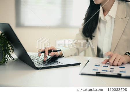 Close up of businesswoman working on laptop and analyzing documents with financial data. 130082708
