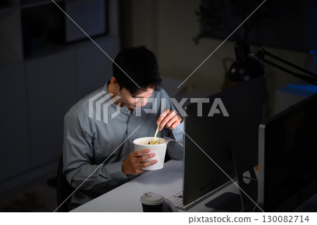 Businessman eating instant noodles while working late night in front of computer Businessman eating instant noodles while working late night in front of computer 130082714