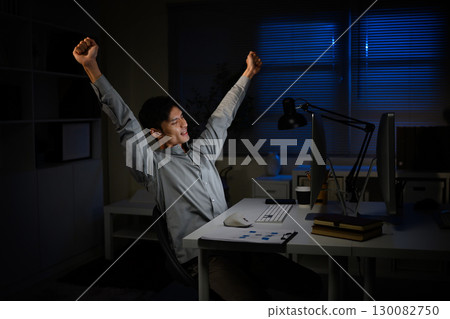 Happy businessman celebrating success while working late night at office desk 130082750