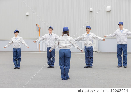 A group of workers doing exercises in front of a factory A group of workers doing exercises in front of a factory 130082924