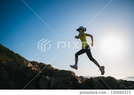 Athletic woman running on sunrise seaside rocks 130084315