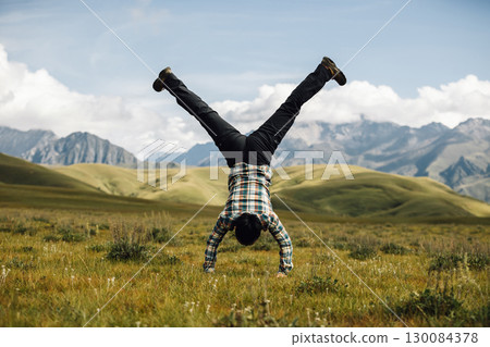 Woman hiker doing a handstand on high altitude mountain top grassland Woman hiker doing a handstand on high altitude mountain top grassland 130084378