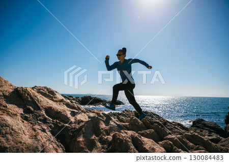 Woman runner running on sunrise seaside rocky mountains Woman runner running on sunrise seaside rocky mountains 130084483