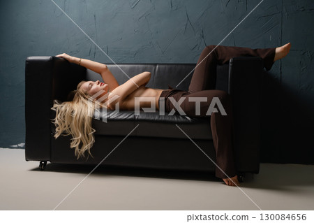 Blonde woman lounges on black couch in stylish studio setting 130084656