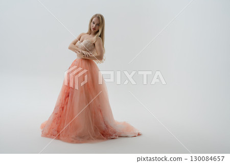 Beautiful woman in a flowing gown poses in a bright studio setting 130084657