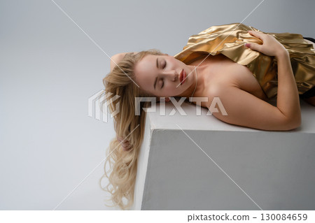 Captivating beauty of a blonde woman in a golden outfit in a studio setting 130084659