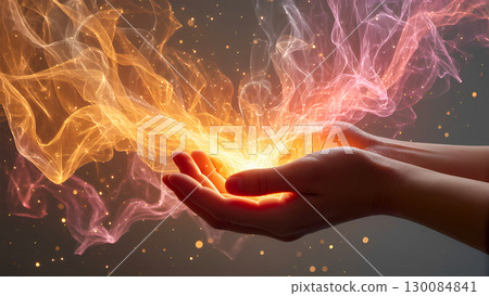 A powerful and mystical image of two cupped hands holding and emitting a glowing, swirling cloud of warm energy and light. The light, a mix of vibrant oranges, reds, and golden hues, rises from the pa 130084841