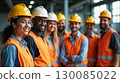 Group of smiling construction workers wearing safety helmets and reflective vests standing together in an industrial environment. 130085022